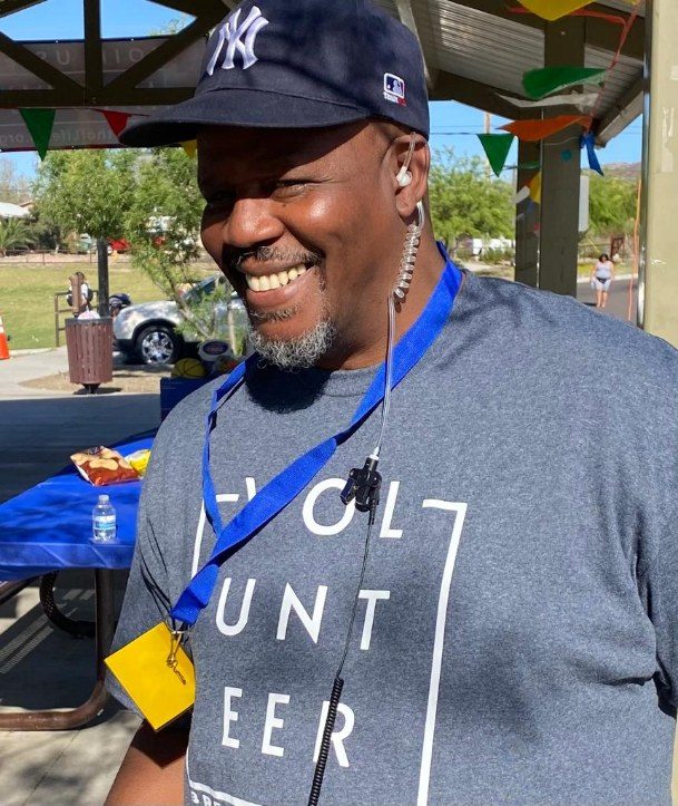 A smiling volunteer in a cap and volunteer shirt