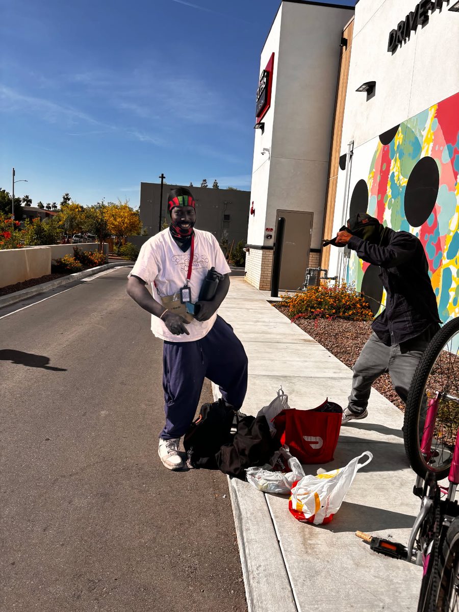 A volunteer sorting bags of supplies on a sidewalk beside a neighbor with a bicycle