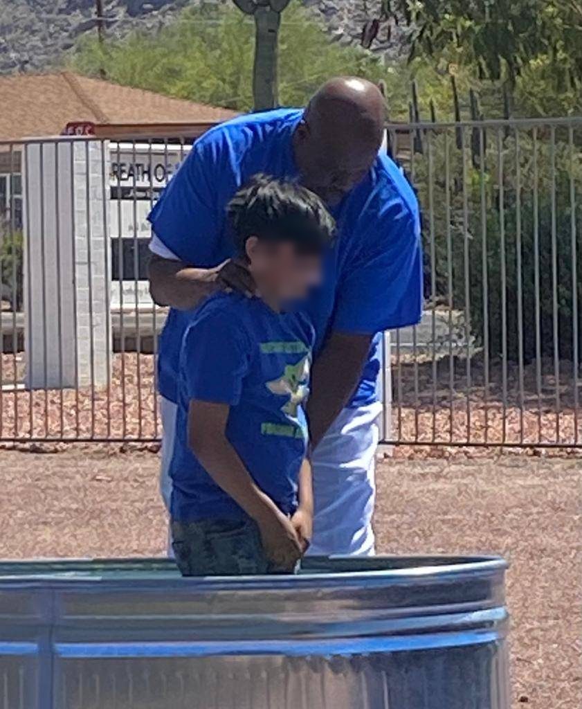A minister in blue guiding a boy during an outdoor baptism